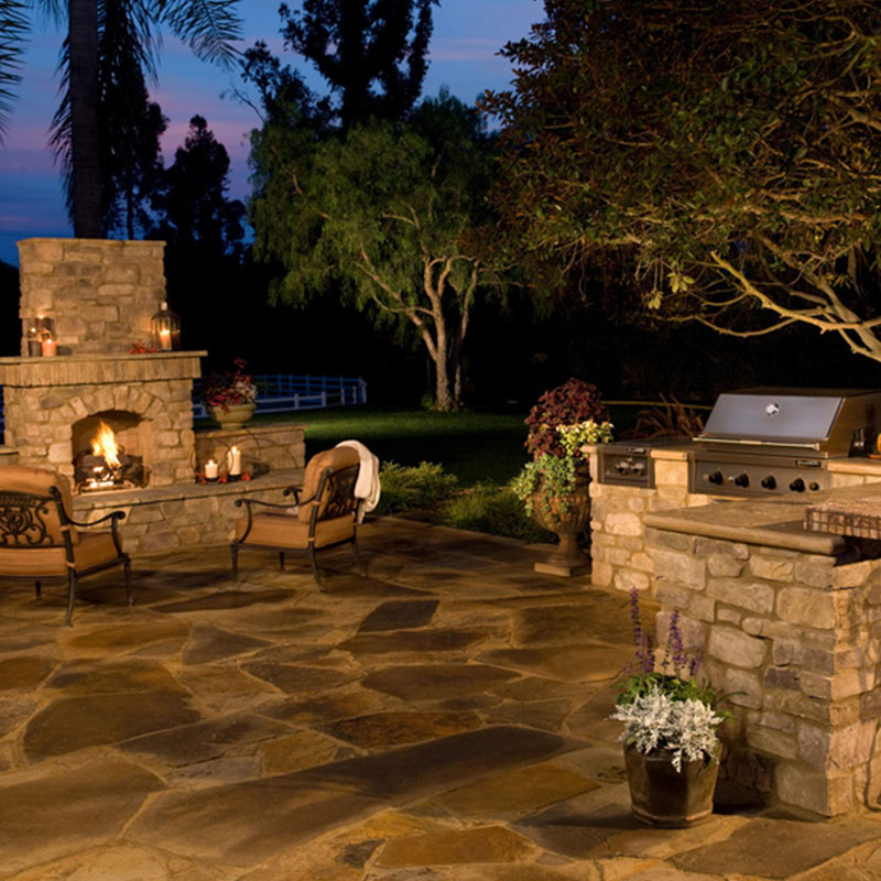 outdoor patio area with an outdoor fireplace and outdoor kitchen in the night time